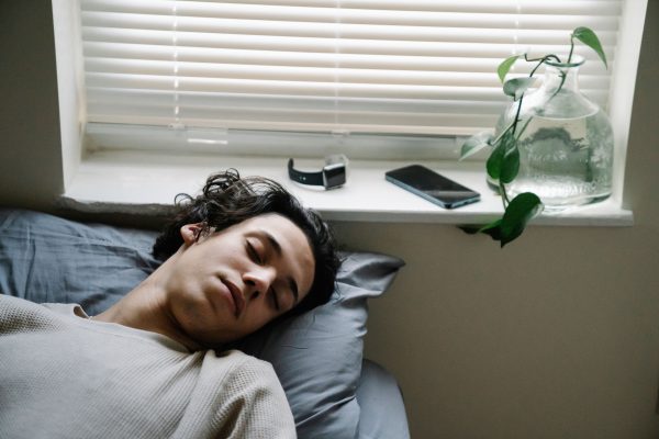 A young man sleeping on a bed with a smartphone and smartwatch on the windowsill.