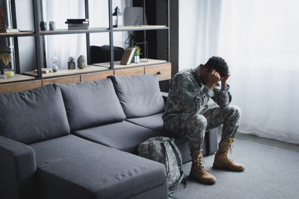 Man in a military uniform sits on a couch with his head in his hands