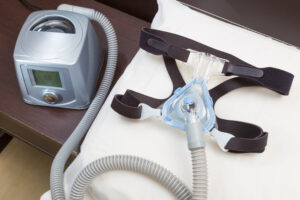 A cpap machine rests on a nightstand and a cpap hose rests on a bed