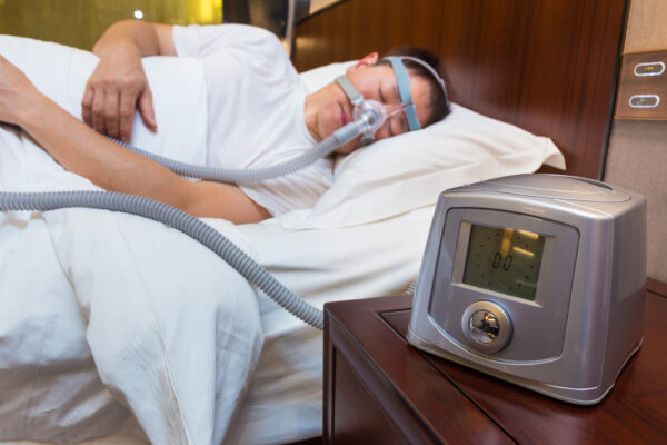 Cpap machine sitting on a table next to a sleeping man with a cpap mask on