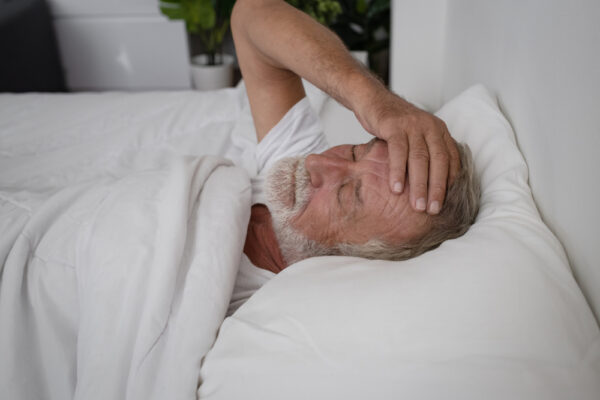 senior man in bed holding his head in pain