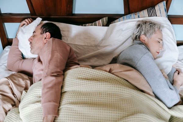 A serene scene of a couple sleeping back to back, nestled under warm blankets.